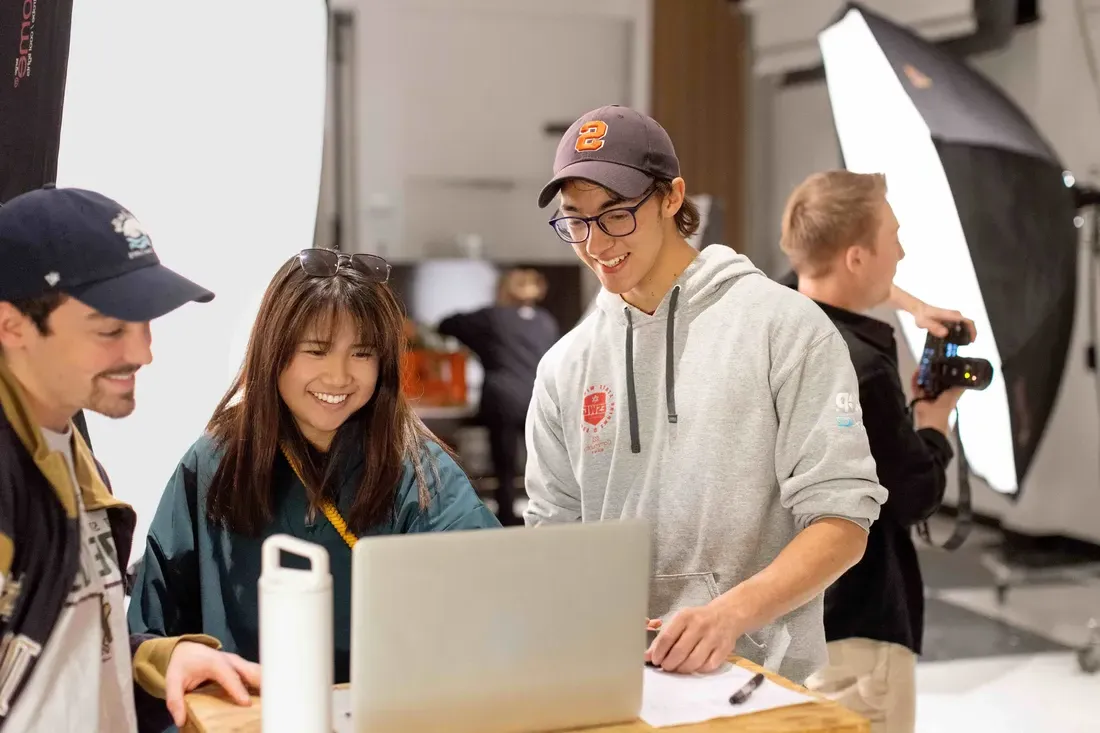 Students smiling and looking at a computer in class.